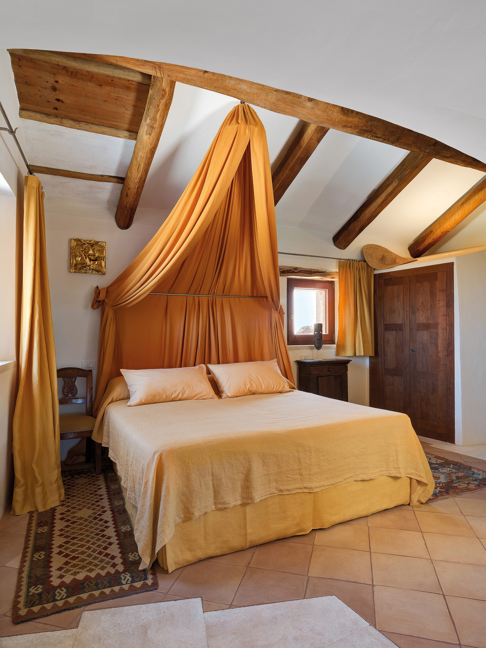 Несколько ступеней ведут из гостиной в главную спальню с кроватью под балдахином из льняной ткани цвета охры.