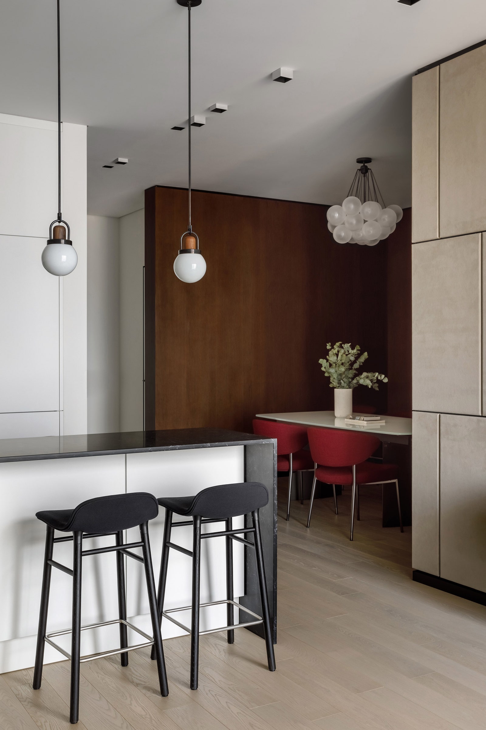 Вид из кухни на столовую со стенами облицованными орехом и креслами винного цвета.