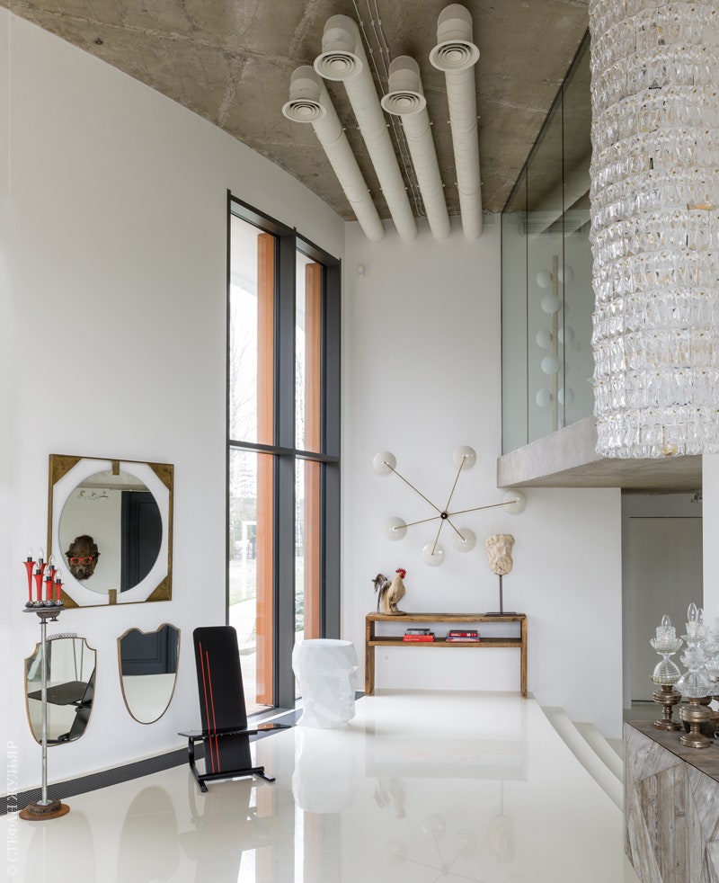 В холле табурет в виде головы Adan Stool Vondom. Красный столик Moooi. Зеркала черный шезлонг и настенный светильник —...