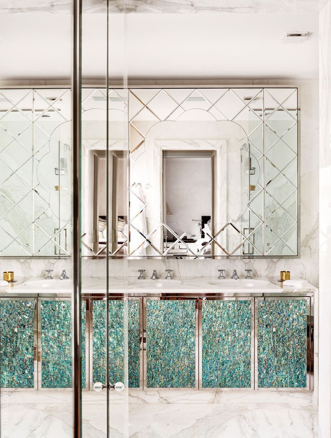 В зеркале ванной комнаты отражается спальня хозяев. Стены и пол отделаны белым мрамором. Зеркало и мебель сделаны на...