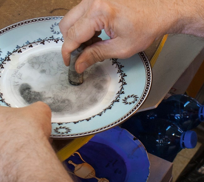 Контуры рисунка переносятся на тарелку с помощью трафарета и тампона с угольной пылью.