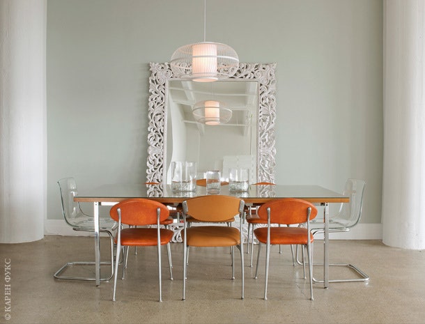 Рыжие стулья вокруг обеденного стола — единственная цветная деталь в интерьере. Зеркало — из Индии.