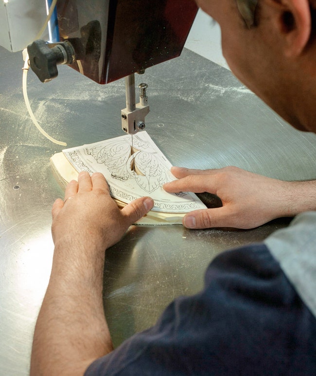 Мастер вырезает элементы для интарсии из листов шпона сложенных в одну стопку.