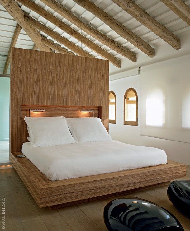 Спальня хозяина. Кровать c высоким деревянным изголовьем сделана на заказ. На переднем плане — фрагмент шезлонга c...