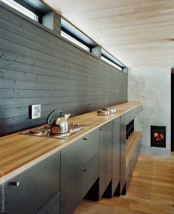Открытая кухня примыкает к зоне столовой. В торце устроена печка из такого же как камин шлифованного бетона.