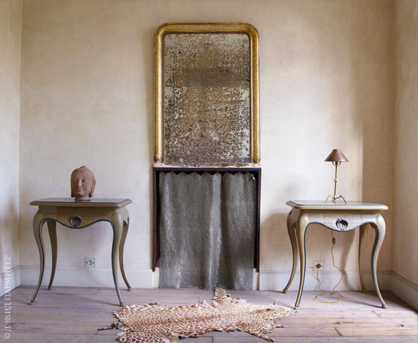 Пара французских столиков XVIII века обрамляет камин портал которого занавешен металлической шторой. Зеркало на стене...
