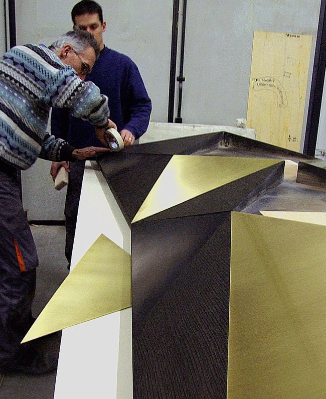 Мастера закреп­ляют медные треугольники на фасадах комода Arlequin.