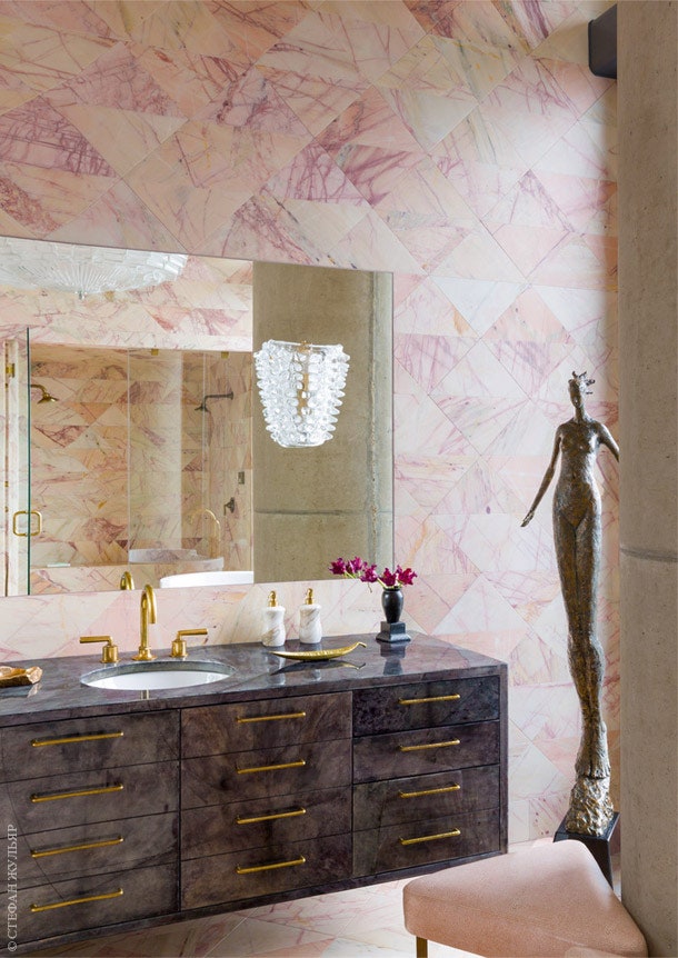 Стены ванной облицованы розовым мрамором тумба под раковину обтянута пергаментом. В зеркале отражается светильник 1960‑х...