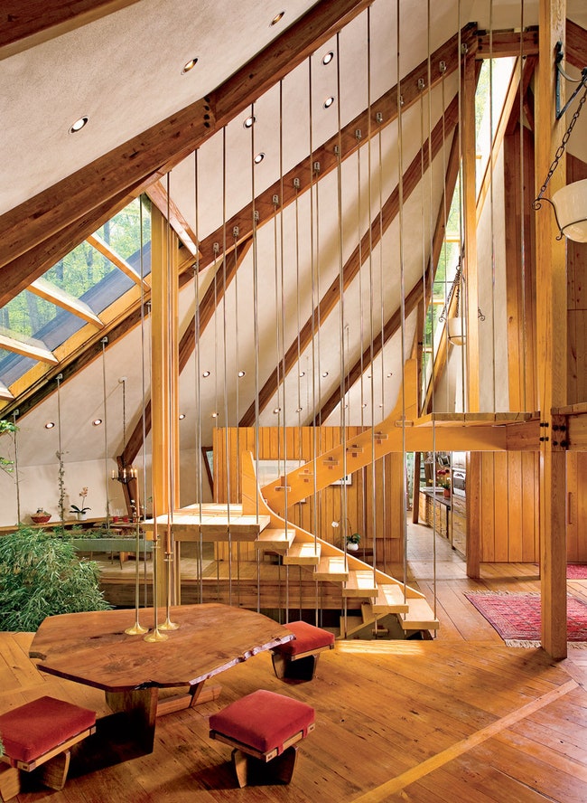 Стальные прутья служат ограждением лестницы и опорой для крыши дома. Деревянный стол и табуретки сделаны по дизайну...