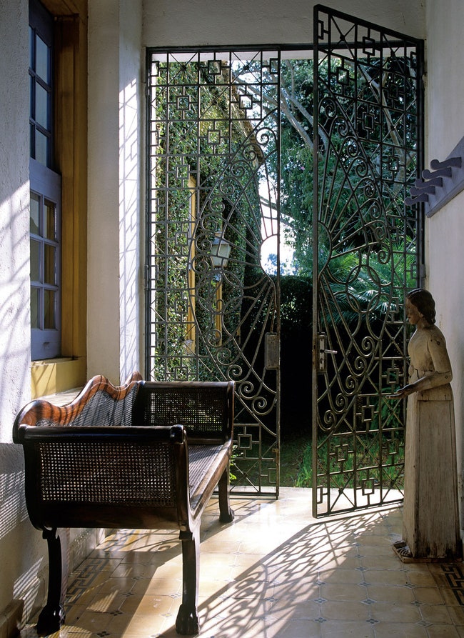 На фоне ажурных ­металлических ворот — плетеный диванчик XIX века из жакаранды.