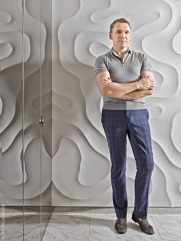 Майк Шилов на фоне гипсовой стены с рельефным коралловым мотивом.