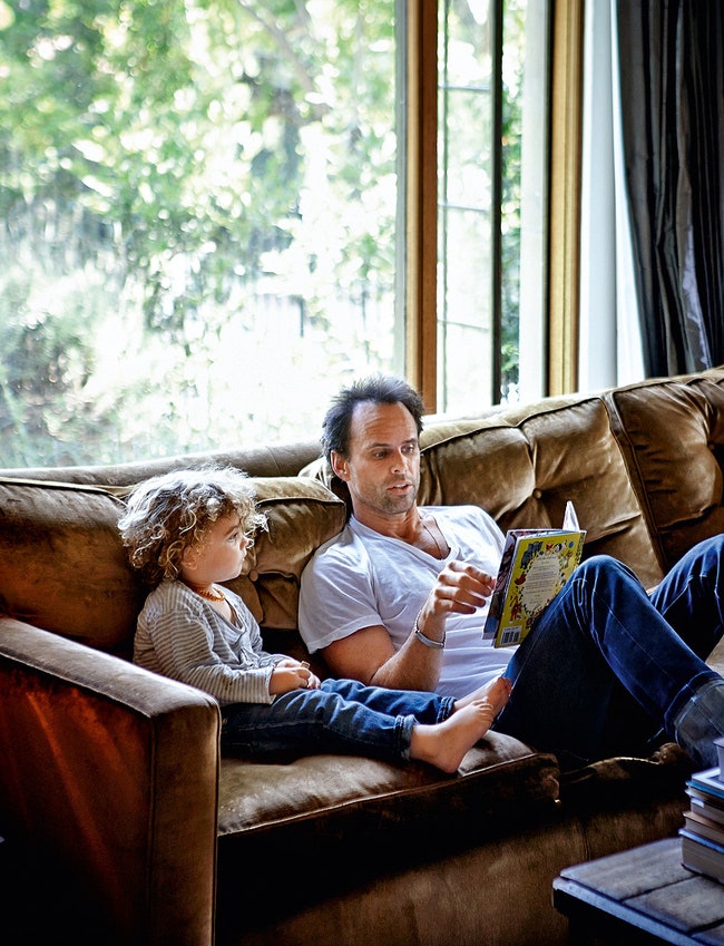 Уолтон Гоггинс на диване в гостиной читает книжку сыну..