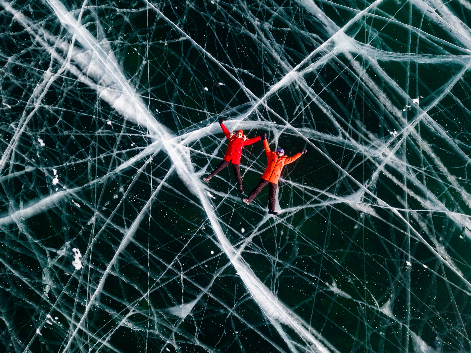 Couple  man and woman in the red jackets is lying on the transparent ice. Baikal aerial view. Olkhon Island Lake Baikal...